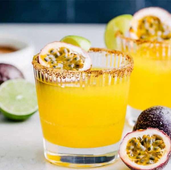 Yellow cocktail with agave vodka in a glass with a passion fruit garnish on a white surface.